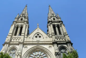 Fachada da Igreja de São Luís em Bordéus com duas torres gémeas góticas pontiagudas, um rosáceo central e elementos arquitetónicos detalhados em pedra branca contra um céu azul.