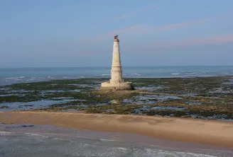 O farol de Cordouan, um farol branco e bege com cúpula vermelha, localizado num rochedo coberto de algas ao largo de Bordéus, rodeado por praias de areia e do oceano Atlântico.