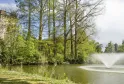 Vista do Parque de Bourran em Bordéus com uma torre de pedra histórica, um lago com fonte, árvores majestosas e vegetação primaveril exuberante.