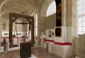 Interior do Museu Nacional das Alfândegas de Bordéus apresentando uma exposição com uma balança histórica em madeira, painéis informativos com fitas vermelhas, retratos e objetos alfandegários em uma galeria abobadada.