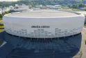 Vista aérea da Arkea Arena, uma arena moderna de formas arredondadas em branco e cinzento, localizada em Floirac perto de Bordéus, com estacionamentos e esplanada de acesso em primeiro plano.